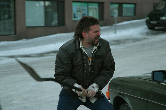 An angry-looking man swinging a shovel towards a car.