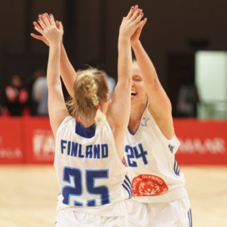 Two basketball players in Finnish national team jerseys give each other a high-five.