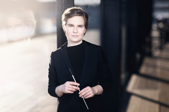 A woman dressed all in black holds a conductor's baton.