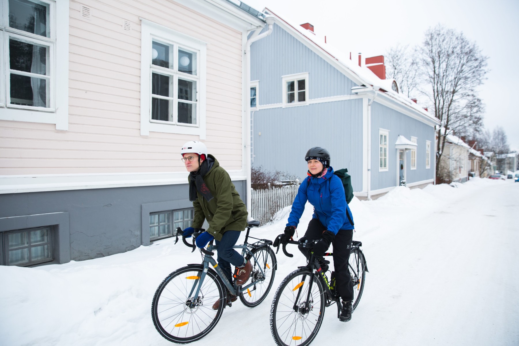A man and a woman bike down a snowy street.