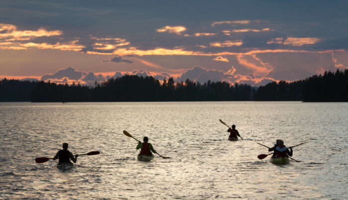 Four kayaks make their way across a lake in the dusky light of evening.