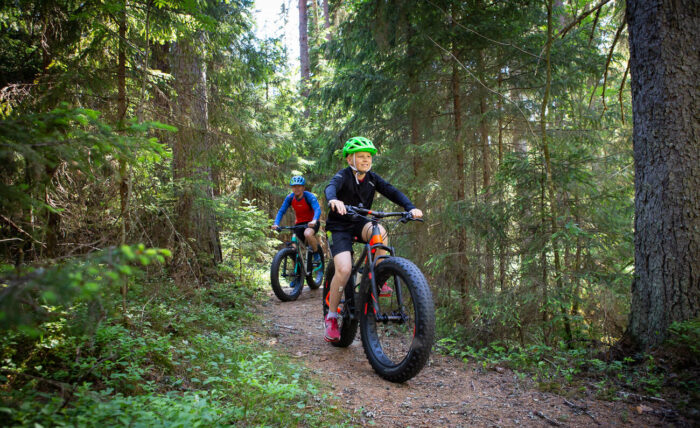 Two young people on fat-tyre bikes ride along a path through a forest.