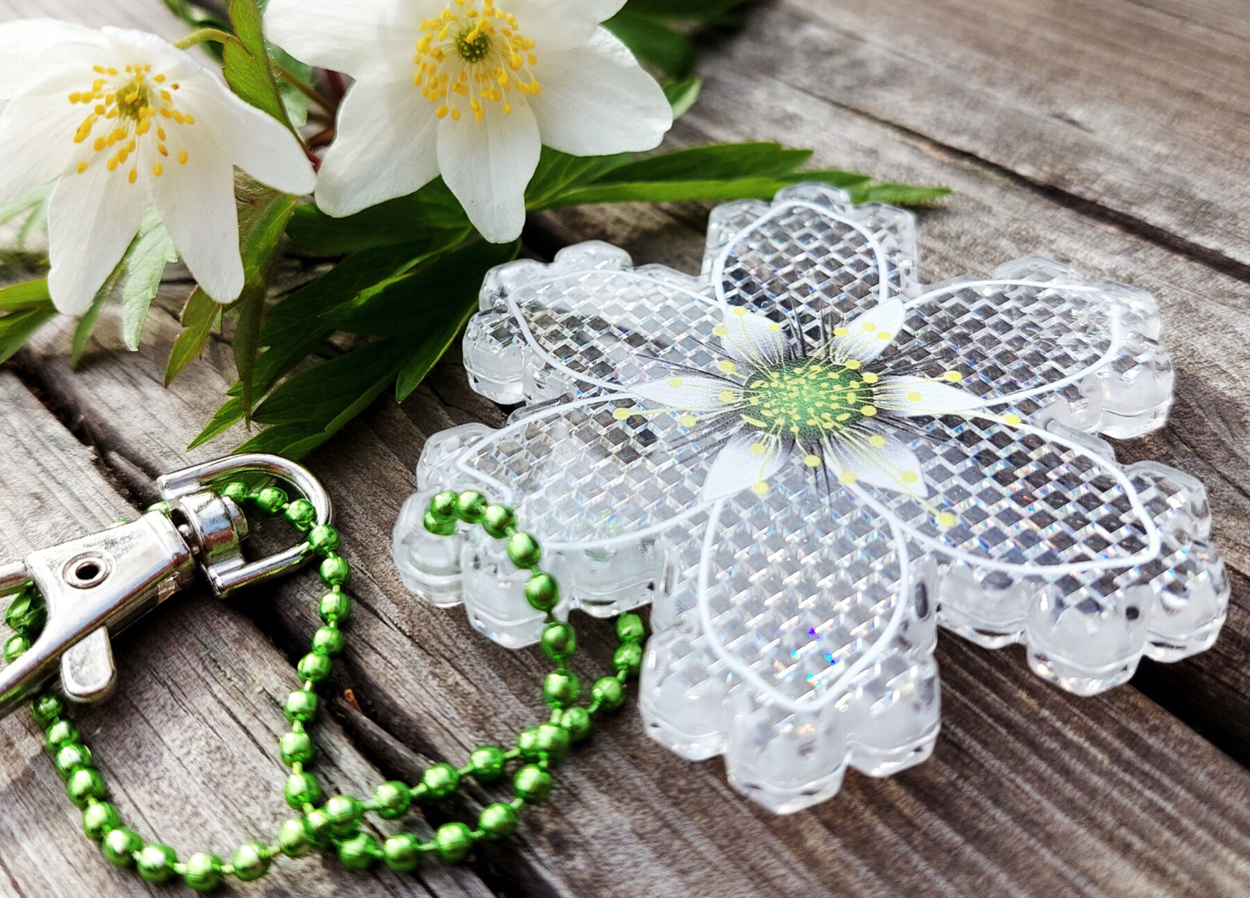 Ein flaches, sechszackiges Stück Kunststoff, das mit Linien versehen ist, um es wie eine Blume aussehen zu lassen, liegt zusammen mit zwei echten Blumen auf einem hölzernen Untergrund.