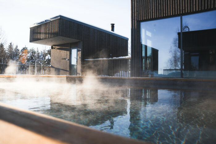 Steam rises off an outdoor pool in front of a modernistic wooden building.