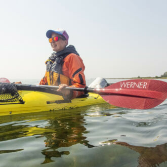 A person sits in a kayak on the water, holding a paddle.