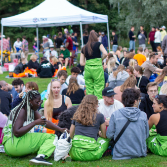 Groups of young people are sitting on a lawn in a park eating, drinking and talking.