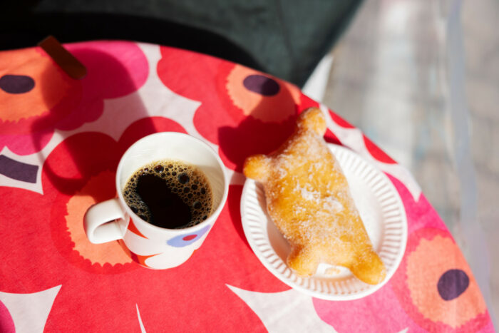 A cup of coffee and an almost rectangular pastry are on a Marimekko floral-pattern tablecloth.