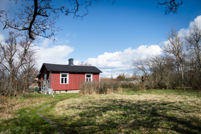 Uma casa vermelha fica em uma clareira arborizada no sul da Finlândia, cercada por árvores desfolhadas no início da primavera.